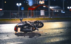 A motorcycle lies on its side in the middle of a wet street at night, suggesting a recent accident. Debris is scattered nearby. - Mereces Jeremías A motorcycle lies on its side in the middle of a wet street at night, suggesting a recent accident. Debris is scattered nearby.