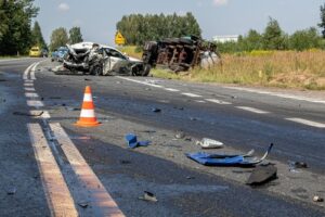 A car and truck are severely damaged after a collision on a rural road, with debris and a traffic cone scattered across the scene.