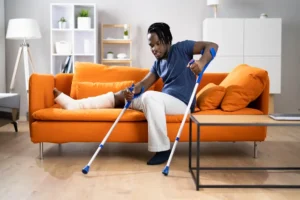 A person with a leg cast sits on an orange sofa, using crutches to stand up in a living room setting. - Mereces Jeremías A person with a leg cast sits on an orange sofa, using crutches to stand up in a living room setting.