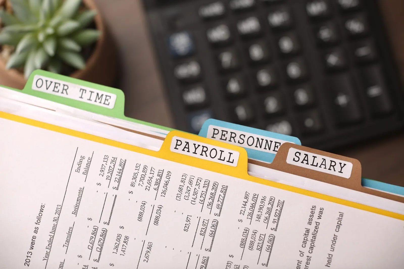 Folders labeled "Over Time," "Payroll," "Personnel," and "Salary" are stacked on a desk next to a calculator and a small plant.