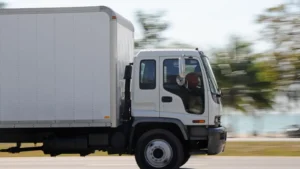 A white box truck driving on a road, with a blurred background indicating motion.