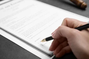 A person holding a pen is about to sign a document placed on a dark surface.