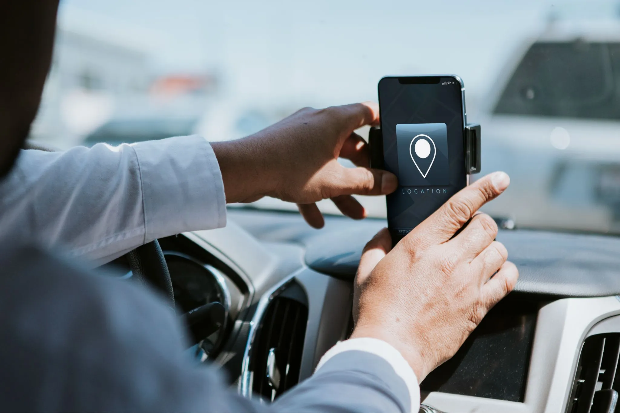 A person sets up a smartphone with a navigation app open, showing a location pin icon, on a car dashboard mount.